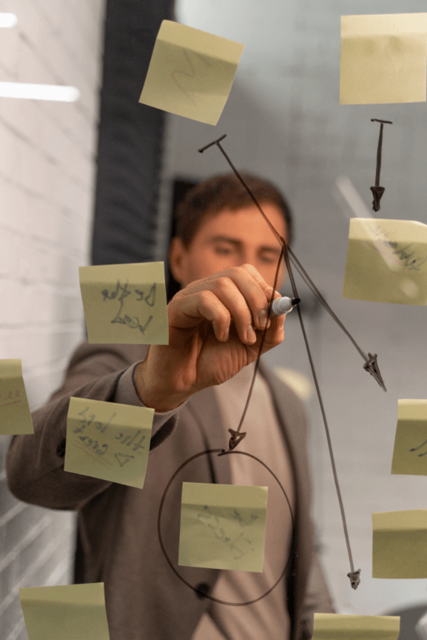 Profissional escrevendo em post-its em um quadro de vidro, simbolizando comunicação clara e objetiva nos processos de gestão