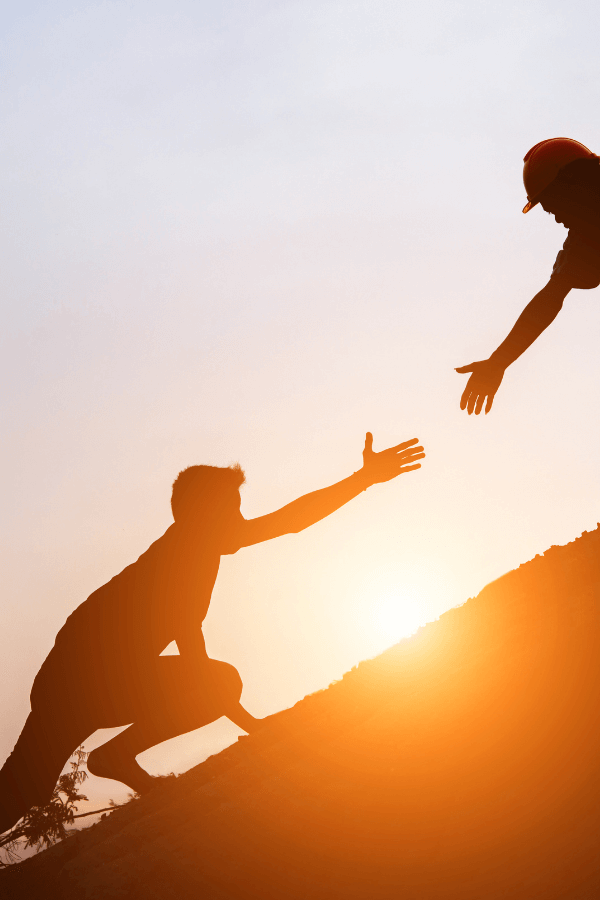 Pessoa ajudando outra a subir uma montanha ao pôr do sol, simbolizando resiliência e apoio mútuo no trabalho em equipe